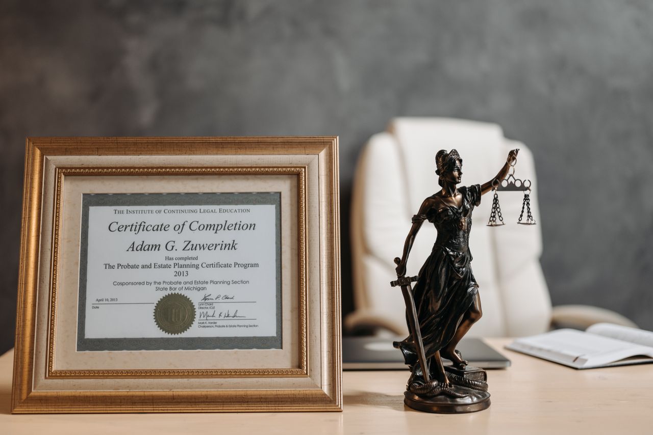 Aree di attività A framed legal certificate and Lady Justice figurine on a desk in a law office setting.